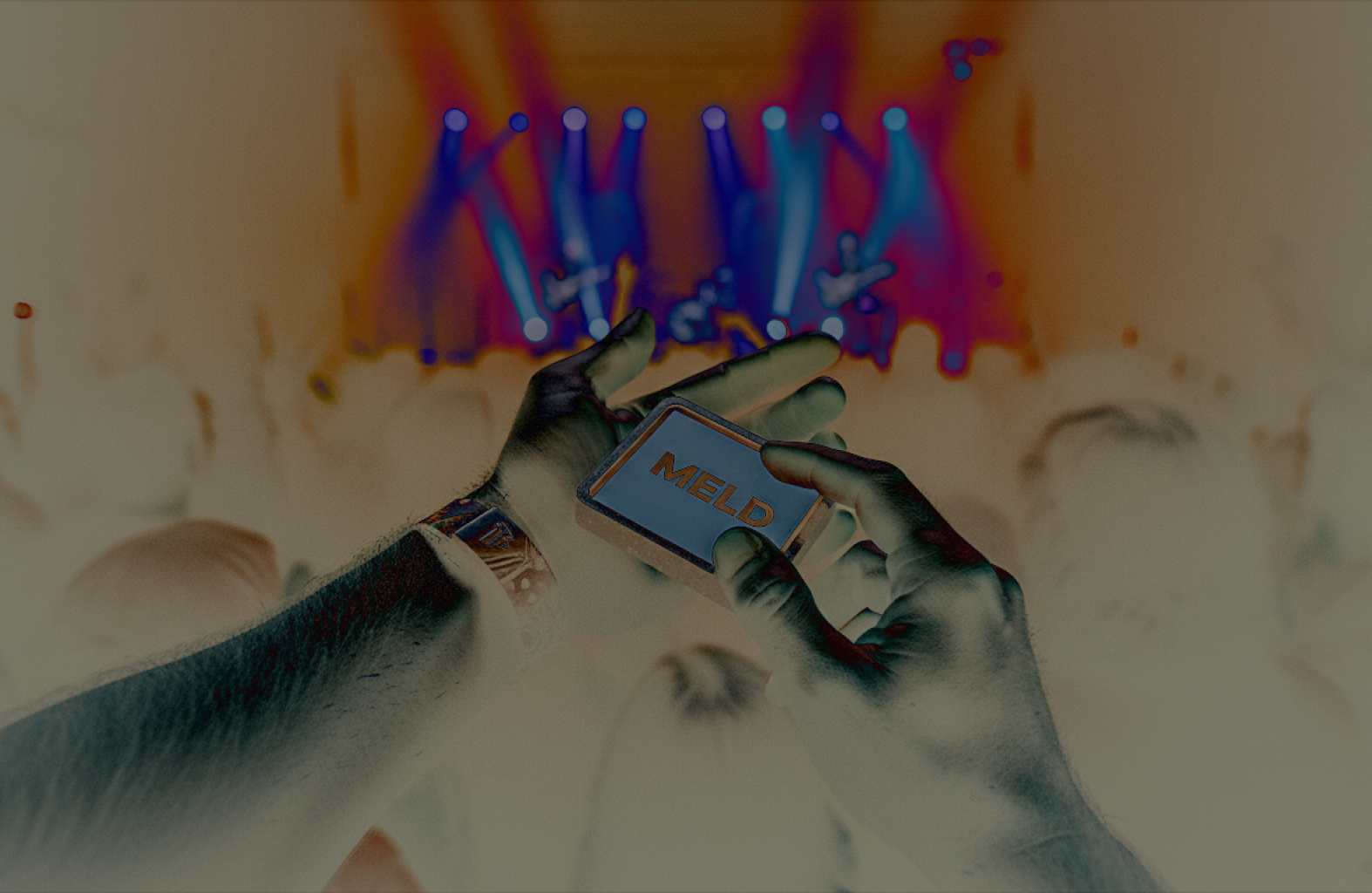 MELD device held in two hands at a live concert, stage lights in the background.